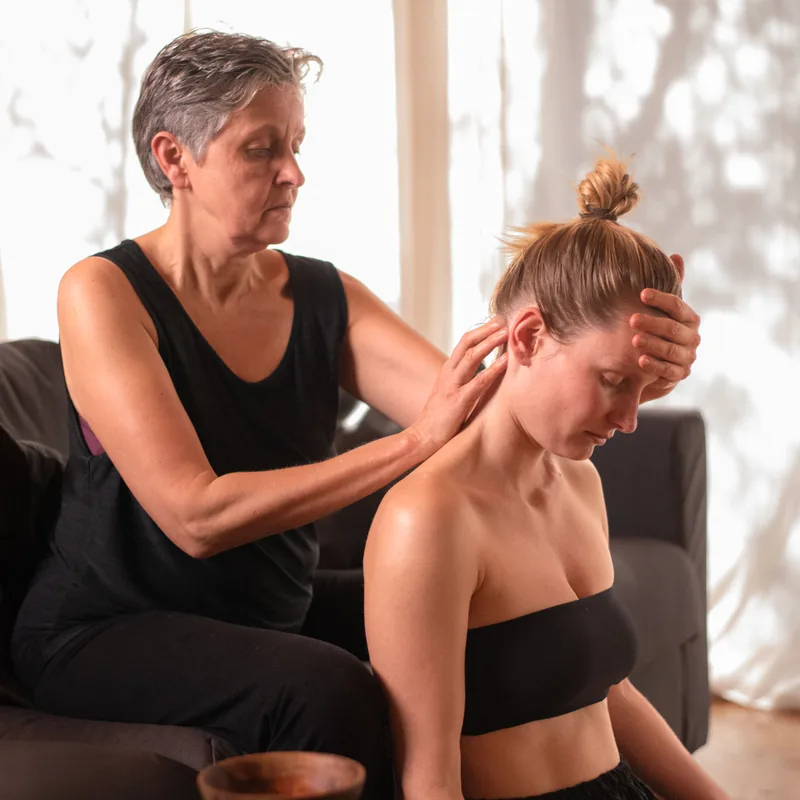 Karuna geeft een nek- en schoudermassage aan iemand die op de grond zit
