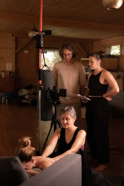 Jonathan en Nicole met geprinte scripts achter de camera, terwijl Karuna voor de lens een massage geeft